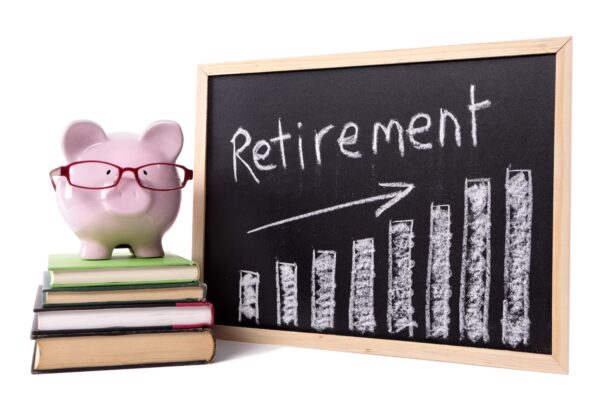 Pink piggy bank with glasses standing on books next to a blackboard with retirement savings chart. Sharp focus on the piggy bank.