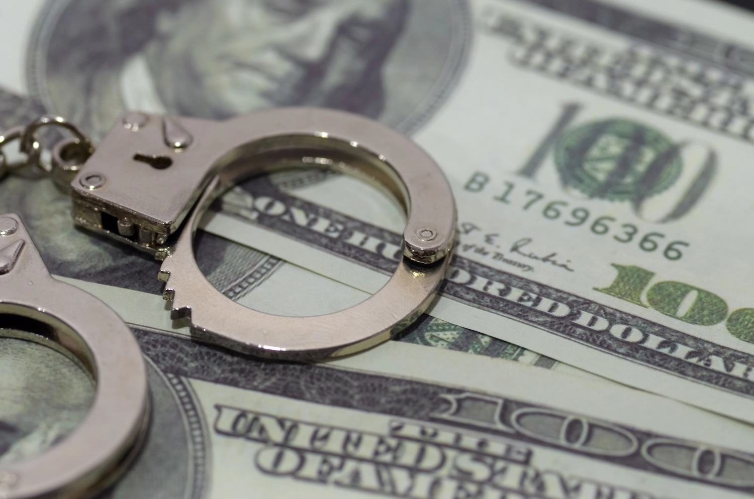 a pair of handcuffs lying on a bed of U.S. dollar bills. This juxtaposition suggests the corrupting influence of money or the potential for financial crimes.