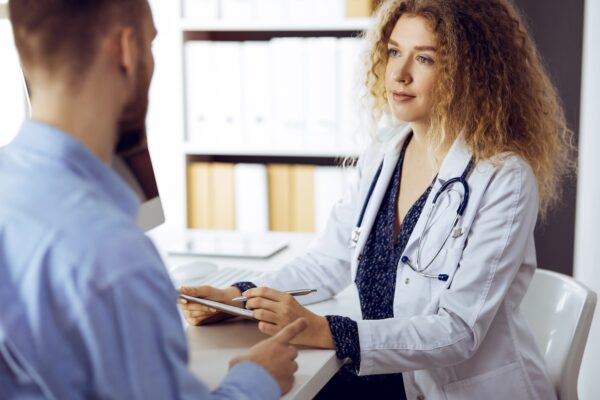 Female dentist and male patient discussing current health examination while sitting in sunny clinic.