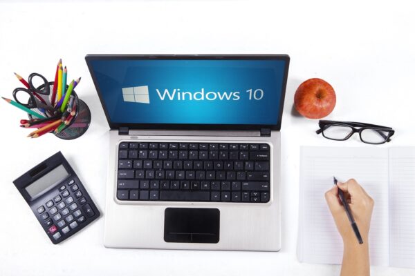 Closeup of a notebook computer with windows 10 logo and a student hand writing on the book