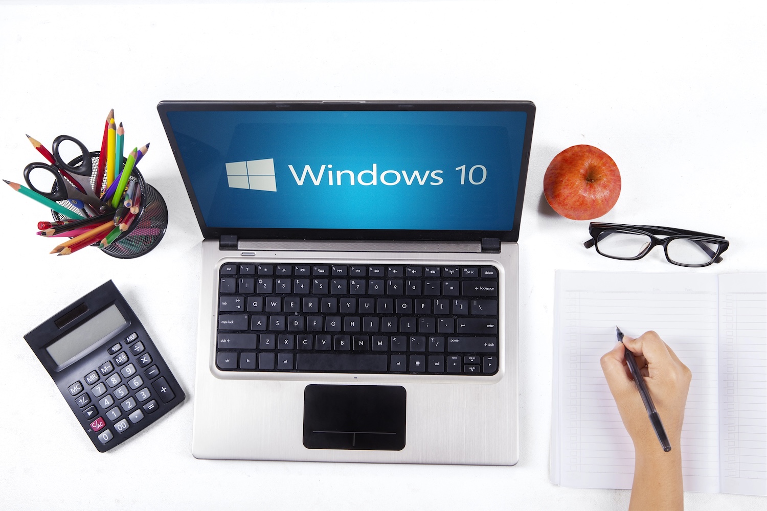 Closeup of a notebook computer with windows 10 logo and a student hand writing on the book