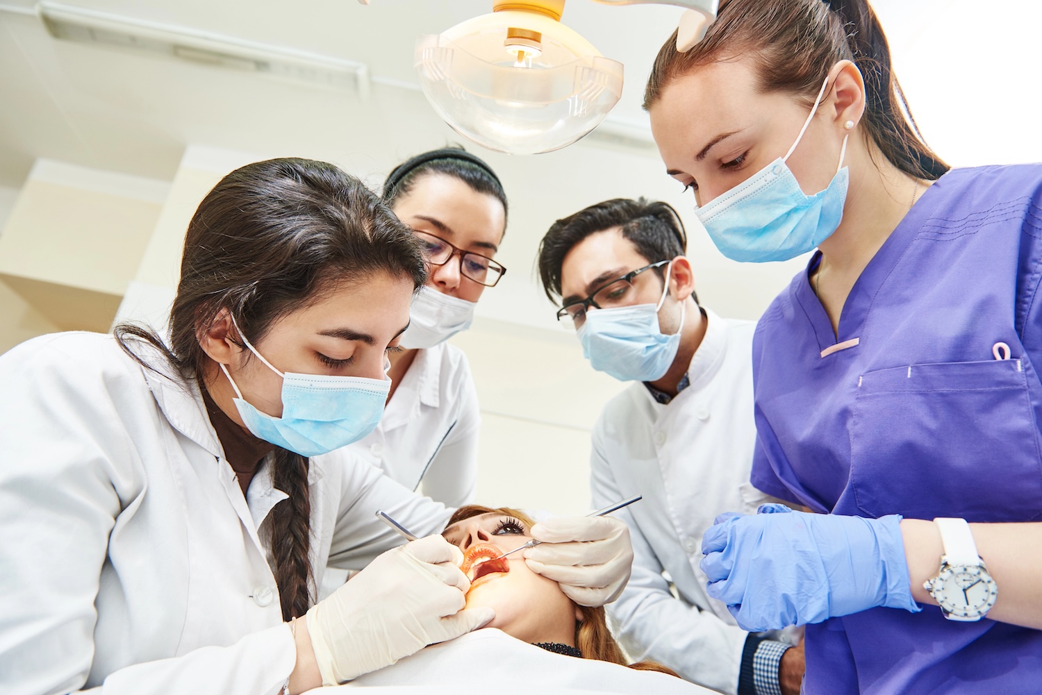 Dentistry education. Female dentist doctor teacher explaining treatment procedure to iranian asian students group in dental clinic