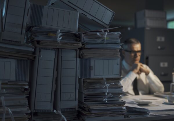 Sad pensive businessman sitting at desk at night and thinking, he is overloaded with paperwork
