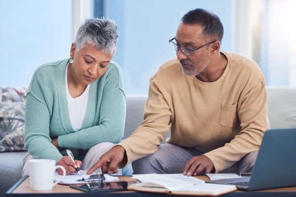 Senior black dentist couple looking at retirement planning docs on laptop