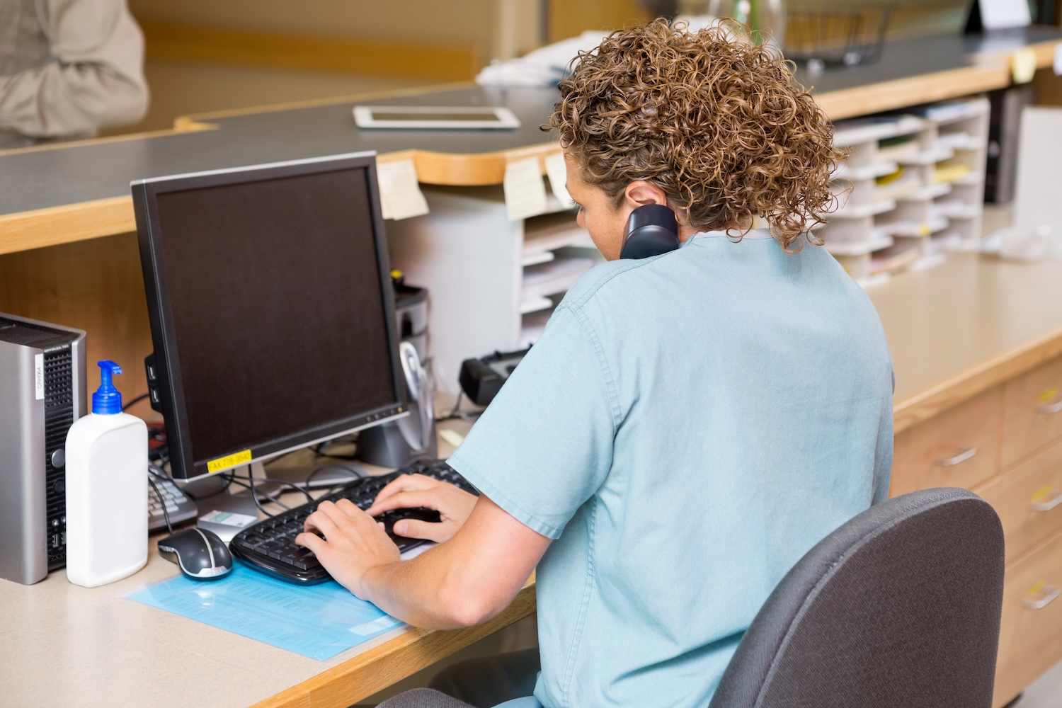 Rear view of receptionist answering telephone while working on computer at dental office reception