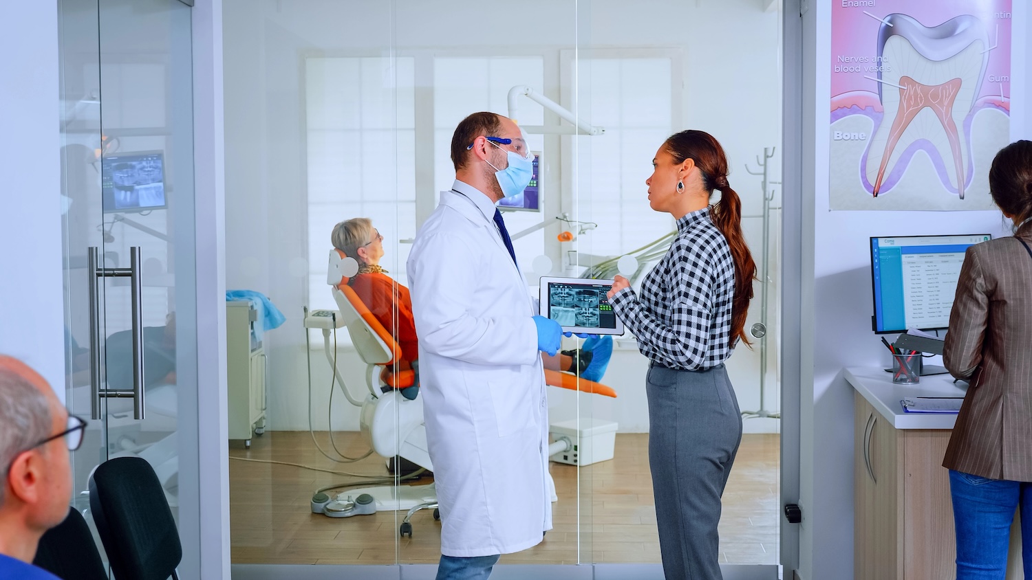 Dentistry showing x-ray of teeth to patient using tablet standing in waiting area of dental clinic . Stomatologist reviewing dental radiography with woman explaining treatment in crowded office